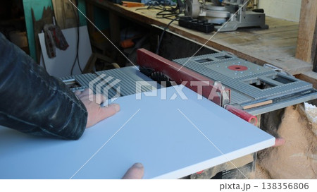 In a woodworking shop, a carpenter clamps a board to the tabletop of a running circular saw to cut a piece, a technique used to cut building materials on a miter saw, cutting material on a power saw In a woodworking shop, a carpenter clamps a board to the tabletop of a running circular saw to cut a piece, a technique used to cut building materials on a miter saw, cutting material on a power saw 138356806