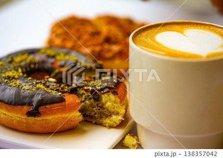 Dubai-style donuts with chocolate glaze topped with chopped pistachios, coffee 138357042