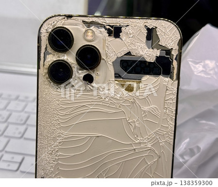 ALMATY, KAZAKHSTAN - FEBRUARY 27, 2025: The back of a broken glass gold side of a broken iPhone 13 Pro displayed on a showcase shelf in an electronics store. Close-up. 138359300