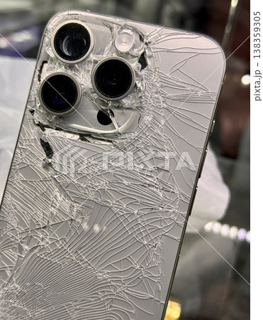 ALMATY, KAZAKHSTAN - FEBRUARY 27, 2025: The back of a broken glass silver side of a broken iPhone 14 Pro displayed on a showcase shelf in an electronics store. Close-up. ALMATY, KAZAKHSTAN - FEBRUARY 27, 2025: The back of a broken glass silver side of a broken iPhone 14 Pro displayed on a showcase shelf in an electronics store. Close-up. 138359305