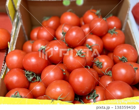 A vibrant display of ripe cherry tomatoes stacked neatly in a yellow basket at a bustling local market. Close-up. 138359410