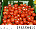 A vibrant display of ripe cherry tomatoes stacked neatly in a green basket at a bustling local market. Close-up. 138359419