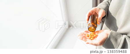 Hand holding brown bottle and pouring yellow vitamins, pills, or capsules into palm, promoting health and wellness. Person pouring yellow supplements into hand. Healthy lifestyle, self-care Hand holding brown bottle and pouring yellow vitamins, pills, or capsules into palm, promoting health and wellness. Person pouring yellow supplements into hand. Healthy lifestyle, self-care 138359488