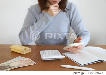 スマホを見ながら家計簿をつける女性 138359674