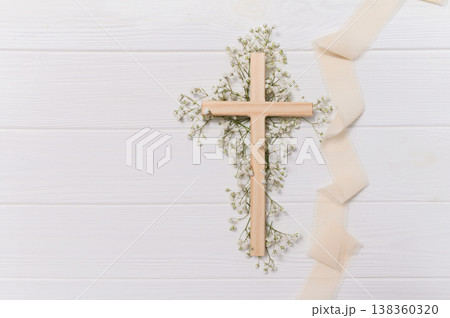 Wooden cross symbolizing christian faith and spirituality, delicate ribbon, and white gypsophila flowers on a clean copy space background remembrance for easter 138360320