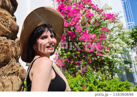 A brunette in a summer hat under the bright sun of Egypt against the backdrop of blooming greenery A brunette in a summer hat under the bright sun of Egypt against the backdrop of blooming greenery 138360696