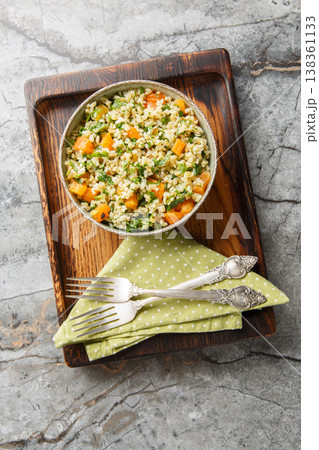 Cooked bulgur mixed with chopped dried apricots and fresh green parsley closeup in a bowl. Vertical top view Cooked bulgur mixed with chopped dried apricots and fresh green parsley closeup in a bowl. Vertical top view 138361133