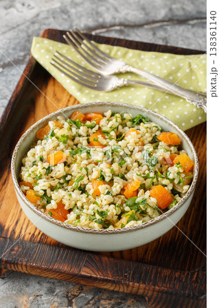 Cooked bulgur mixed with chopped dried apricots and fresh green parsley closeup in a bowl. Vertical Cooked bulgur mixed with chopped dried apricots and fresh green parsley closeup in a bowl. Vertical 138361140