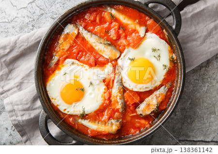 Delicious fried eggs with sardines in vegetable tomato sauce close-up in a frying pan. Horizontal top view Delicious fried eggs with sardines in vegetable tomato sauce close-up in a frying pan. Horizontal top view 138361142