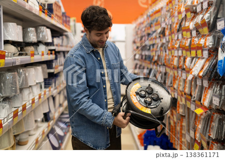 Man holding an extension cord reel, shopping for electrical equipment in a hardware store Man holding an extension cord reel, shopping for electrical equipment in a hardware store 138361171