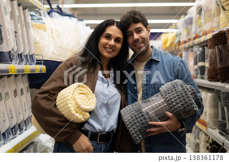 Young couple holding rolled blankets and smiling while shopping in a retail store 138361178