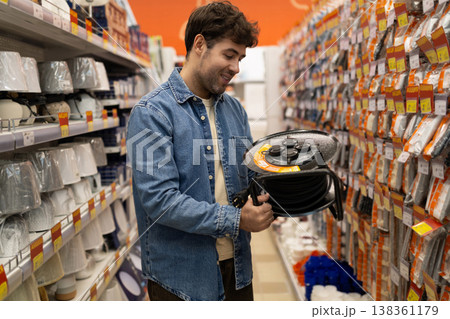 Man holding an extension cord reel, shopping for electrical supplies at a hardware store 138361179