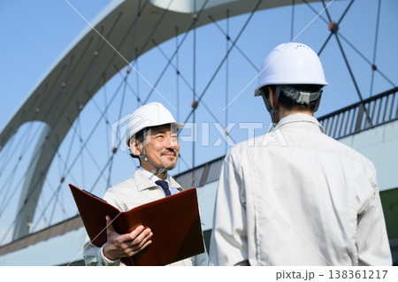 橋を背景に打ち合わせをする作業服の日本人男性 138361217