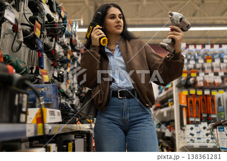 Woman standing in a hardware store aisle comparing two power drills for a diy project 138361281