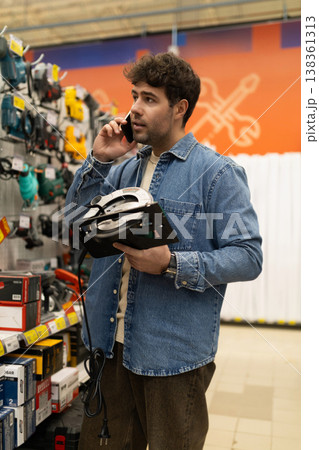 Young man shopping for power tools, talking on smartphone in hardware store Young man shopping for power tools, talking on smartphone in hardware store 138361313