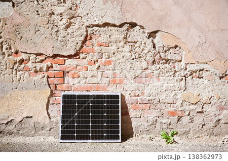 Photovoltaic solar panel at weathered, textured wall with peeling paint. Juxtaposition of modern renewable energy technology against rustic, decaying backdrop highlights contrast between old and new. Photovoltaic solar panel at weathered, textured wall with peeling paint. Juxtaposition of modern renewable energy technology against rustic, decaying backdrop highlights contrast between old and new. 138362973