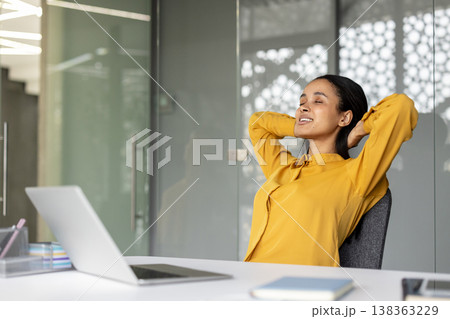 Content young businesswoman enjoying a moment of relaxation and peace, stretching at her office desk with a laptop, finding balance and stress relief during a busy workday Content young businesswoman enjoying a moment of relaxation and peace, stretching at her office desk with a laptop, finding balance and stress relief during a busy workday 138363229
