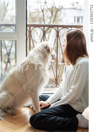 Woman and golden retriever dog sitting by balcony door 138363752