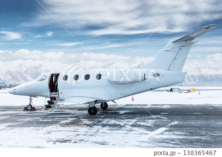 Modern white bizjet with an opened gangway door at the winter airport on the background of high picturesque snow capped mountains Modern white bizjet with an opened gangway door at the winter airport on the background of high picturesque snow capped mountains 138365467