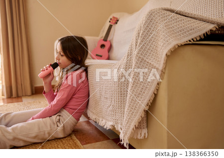 Young Girl Singing Into Toy Microphone Sitting By Sofa With Pink Ukulele Nearby Young Girl Singing Into Toy Microphone Sitting By Sofa With Pink Ukulele Nearby 138366350