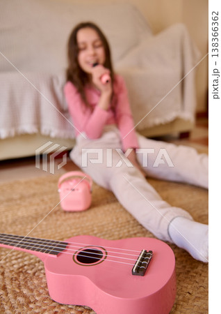 Young Girl Singing With Pink Ukulele At Home On Rug, Playful Childhood Music Time Young Girl Singing With Pink Ukulele At Home On Rug, Playful Childhood Music Time 138366362