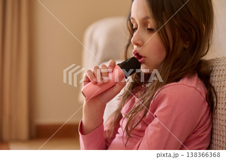 Girl Singing into Pink Microphone While Sitting on Sofa at Home 138366368