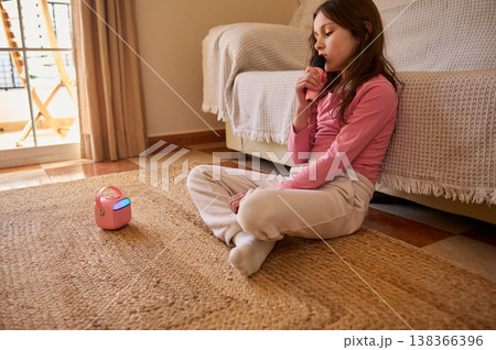 Young Girl Singing Karaoke At Home With Portable Speaker On Living Room Floor 138366396