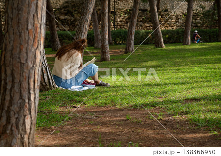 A girl reads a book in the park under a tree 138366950