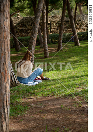 A girl reads a book in the park under a tree A girl reads a book in the park under a tree 138366951