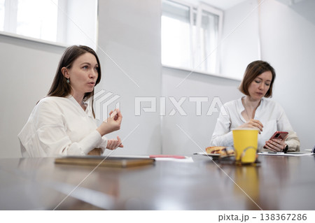 Two women talking side by side at desk with coffee and orange juice during work discussion. Talking, desk, juice, coffee, work, discussion, women. Two women talking side by side at desk with coffee and orange juice during work discussion. Talking, desk, juice, coffee, work, discussion, women. 138367286