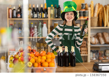 Positive friendly girl seller in traditional green Irish cap offers to buy Irish ale for St. Patrick Day celebration 138367350