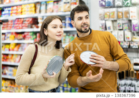 Couple of shoppers are choosing canned fish in food store 138367396