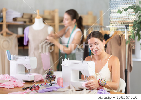Woman seamstress operating by sewing machine. Assistant work with mannequin in background Woman seamstress operating by sewing machine. Assistant work with mannequin in background 138367510