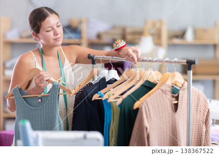 Young dressmaker taking finished dress from rack Young dressmaker taking finished dress from rack 138367522