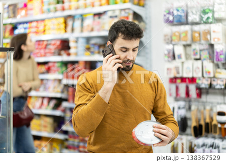 In store, man examines tin can product and talks on phone, advises on purchase. In store, man examines tin can product and talks on phone, advises on purchase. 138367529