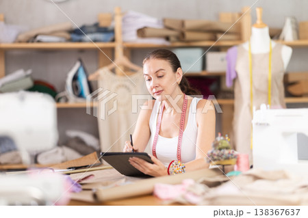 Young female dressmaker drawing on tablet in sewing workshop Young female dressmaker drawing on tablet in sewing workshop 138367637