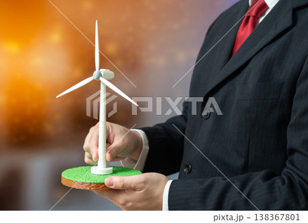 A businessman holds a wind turbine representing energy investment. Renewable systems support autonomy. Sustainable power, infrastructure development, green business strategies energy independence A businessman holds a wind turbine representing energy investment. Renewable systems support autonomy. Sustainable power, infrastructure development, green business strategies energy independence 138367801