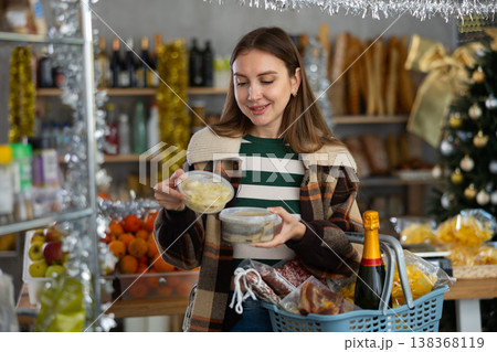Preparing for Christmas celebration - girl chooses salted herring in produce section of supermarket Preparing for Christmas celebration - girl chooses salted herring in produce section of supermarket 138368119