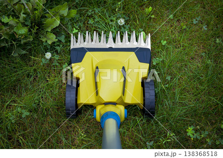 Yellow electric trimmer is cutting the green grass and wildflowers in garden Yellow electric trimmer is cutting the green grass and wildflowers in garden 138368518