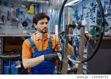 Professional worker adjusting bike wheel in busy workshop setting Professional worker adjusting bike wheel in busy workshop setting 138368733