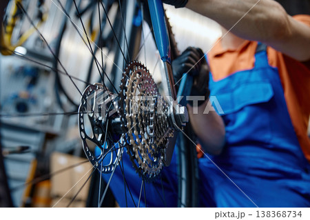 Expert technician carefully adjusting gear system on bicycle in cluttered workspace 138368734