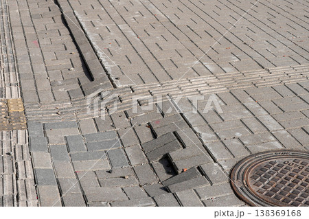 Damaged pavement with displaced paving stones and manhole cover on urban sidewalk surface 138369168