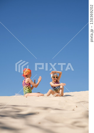 Funny girls are playing and having fun sitting on the sand on the beach. A high sandy mountain of the desert against the blue sky on a hot summer day. Tourism and recreation Funny girls are playing and having fun sitting on the sand on the beach. A high sandy mountain of the desert against the blue sky on a hot summer day. Tourism and recreation 138369202
