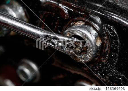 Close up of shiny metal wrench tightening greasy bolt on dark mechanical part, showing detailed texture and wear, industrial maintenance and repair concept Close up of shiny metal wrench tightening greasy bolt on dark mechanical part, showing detailed texture and wear, industrial maintenance and repair concept 138369608