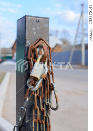 Old rusty chain with padlocks and carbines on a metal pole. Old rusty chain with padlocks and carbines on a metal pole. 138370143