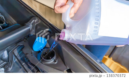 Person pouring liquid into car engine coolant reservoir, close-up view of hand and container, automotive maintenance in progress Person pouring liquid into car engine coolant reservoir, close-up view of hand and container, automotive maintenance in progress 138370372
