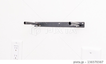 Black metal shelf bracket with level markings attached to white wall near electrical outlet. Home improvement, installed hardware, DIY shelf preparation, wall fixture. 138370387
