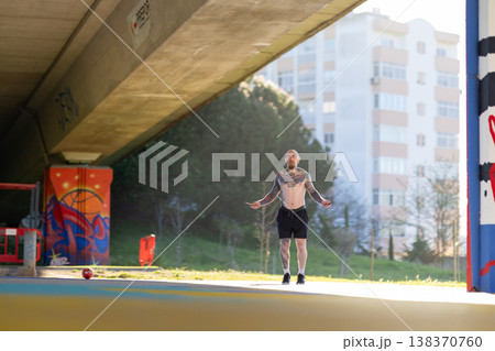 Tattooed man skipping rope training under city bridge 138370760