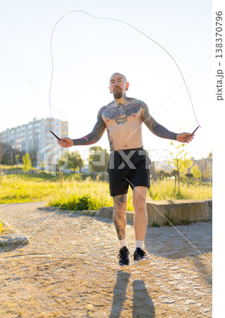 Tattooed man jumping rope doing outdoor workout Tattooed man jumping rope doing outdoor workout 138370796