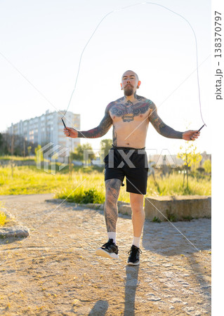 Tattooed man skipping rope exercising outdoors Tattooed man skipping rope exercising outdoors 138370797